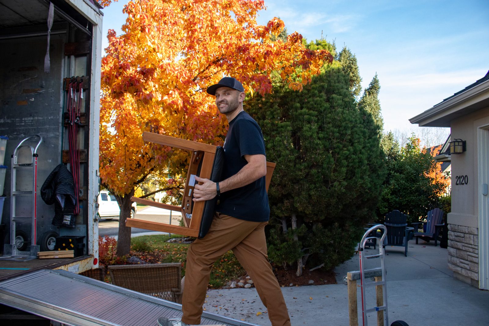 Ace Movers crew member carrying a chair down the truck ramp on a sunny fall day